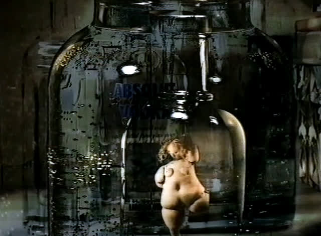 A small clay figure of a woman stands inside a glass Absolut bottle.