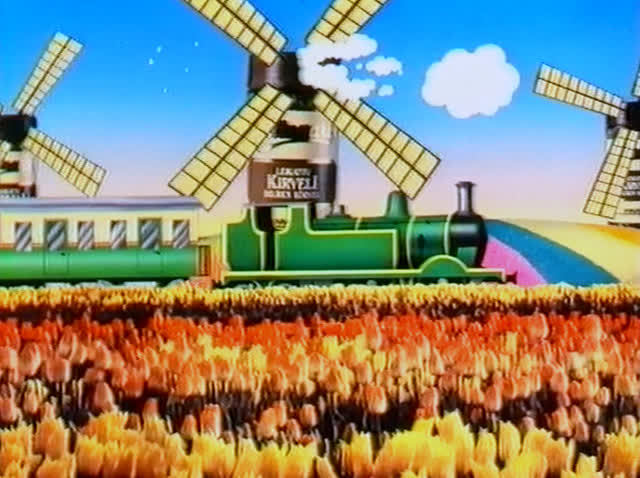 Two windmills stand behind the green train above the wide flower field.