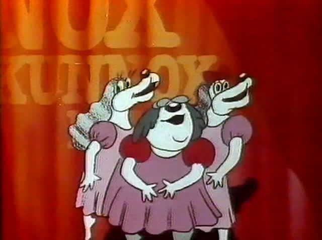A long-snouted dog in a green jacket and cap dances alone in a spotlight.