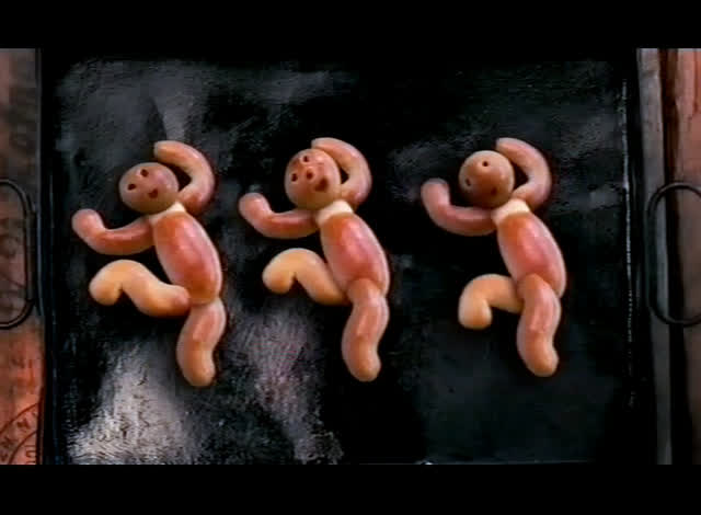Three dough figures with dotted faces lie on a dark baking tray.
