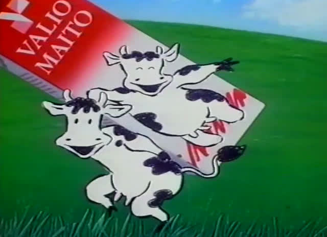 Two drawn cows tumble out of a tilted red Valio Maito carton over green field.
